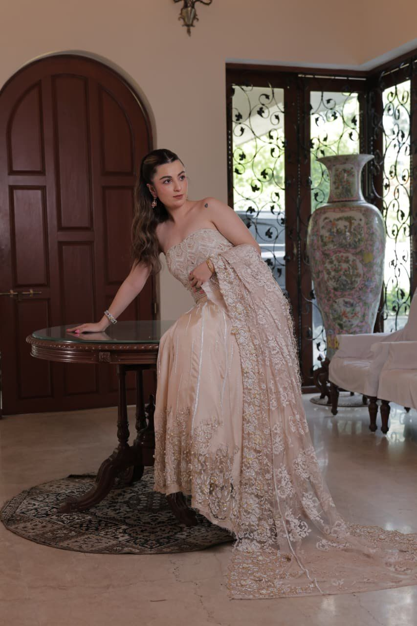 Bride seated in a bespoke blush bridal gown with an embroidered train at a Pune atelier