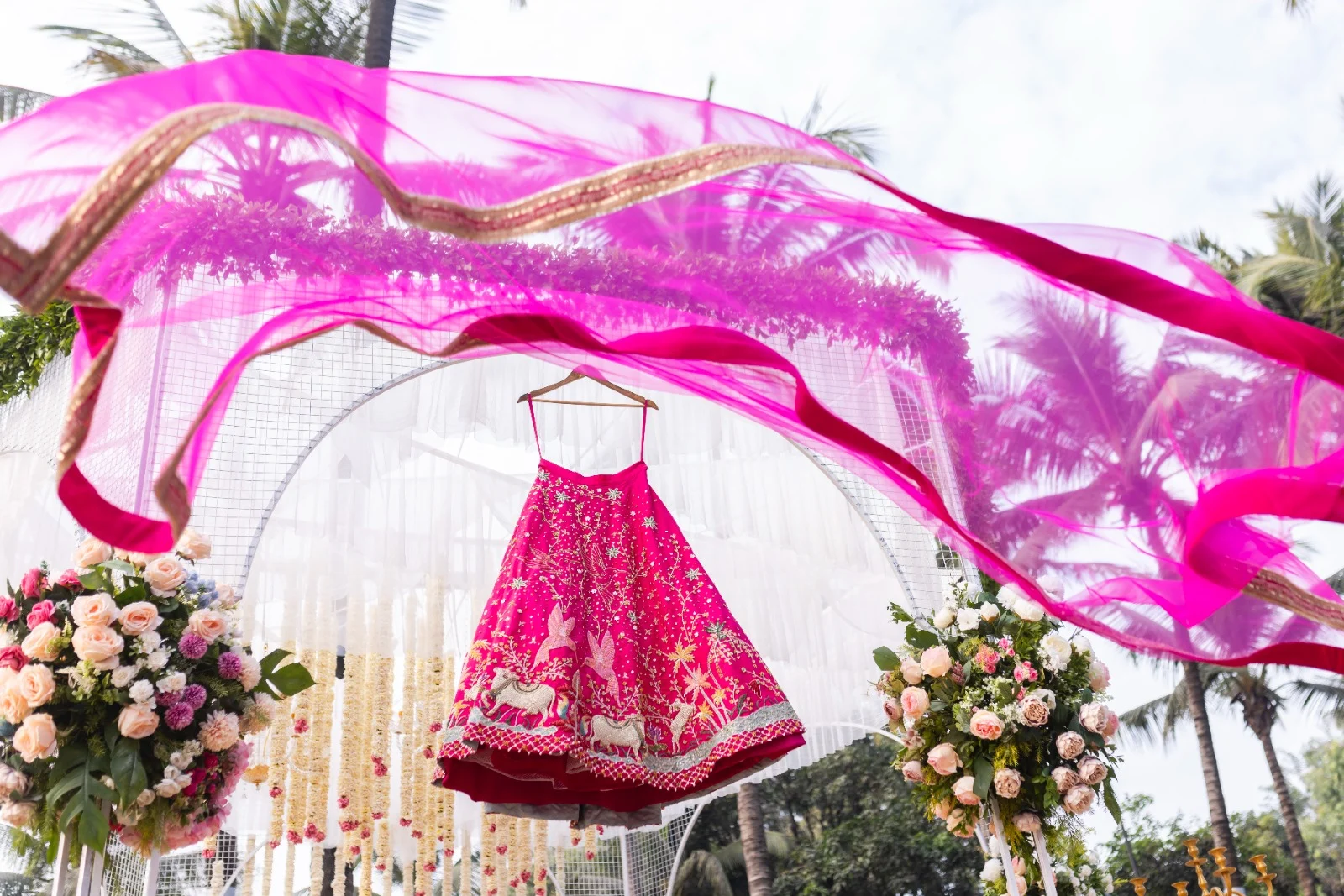 Magenta bridal lehenga with gold embroidery displayed beneath a flowing dupatta at a floral mandap
